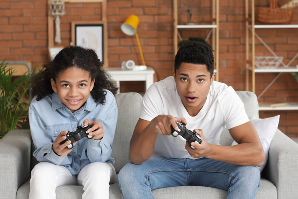 Hermano y hermana afroamericanos jugando videojuegos en casa - Foto, Imagen