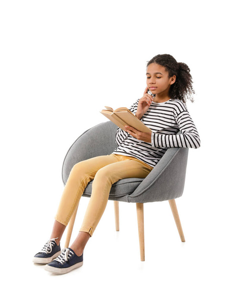 Afro-Amerikaans meisje met boek zittend in fauteuil op witte achtergrond - Foto, afbeelding