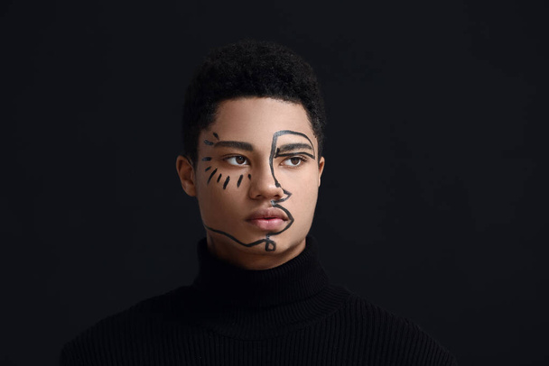 Nuori afroamerikkalainen kaveri, jolla on maali kasvoilla tummaa taustaa vasten - Valokuva, kuva