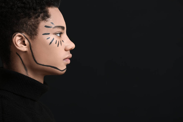 Jonge Afro-Amerikaanse man met verf op gezicht tegen donkere achtergrond - Foto, afbeelding