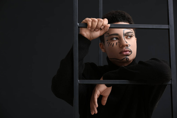 Young African-American guy with paint on face against dark background - Foto, Imagen