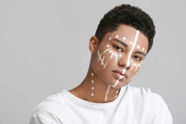 Young African-American guy with paint on face against light background - Zdjęcie, obraz