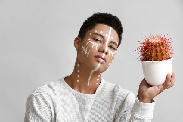 Młody Afroamerykanin z farbą na twarzy i kaktusami na jasnym tle - Zdjęcie, obraz