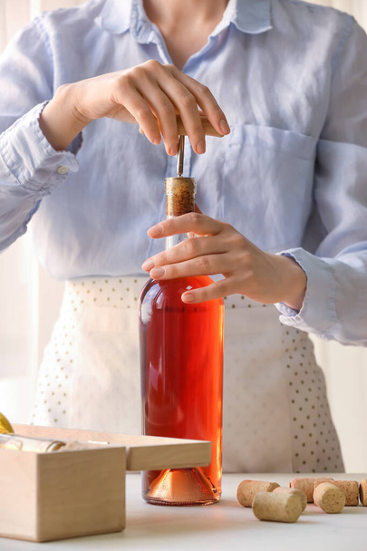 Kobieta otwierająca butelkę wina przy stole - Zdjęcie, obraz