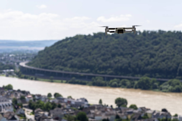 Το drone αιωρείται πάνω από τους λόφους σταφυλιών και την ύπαιθρο, οι πλαστικές προπέλες είναι αναμμένες και η κάμερα στο gimbal είναι ορατή. - Φωτογραφία, εικόνα