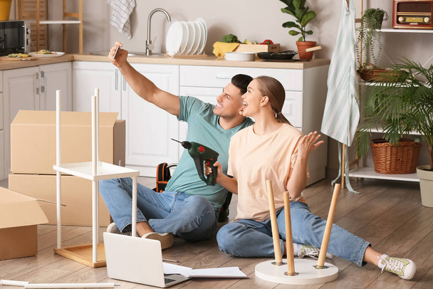 Young couple taking selfie while assembling furniture at home - 写真・画像