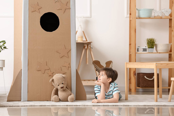 Cute little boy with playing with cardboard rocket at home - Photo, Image