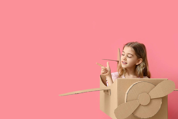 Klein meisje met kartonnen vliegtuigje wijzend naar iets op kleur achtergrond - Foto, afbeelding