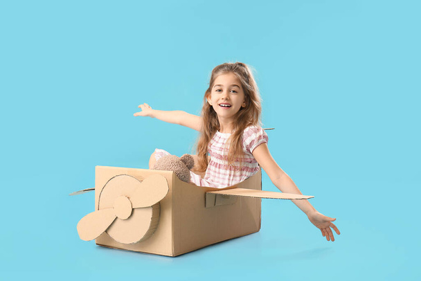 Little girl playing with cardboard airplane on color background - Photo, Image