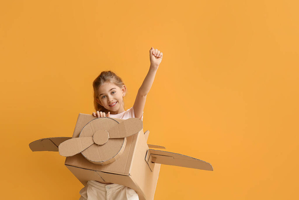 Little girl playing with cardboard airplane on color background - Фото, изображение