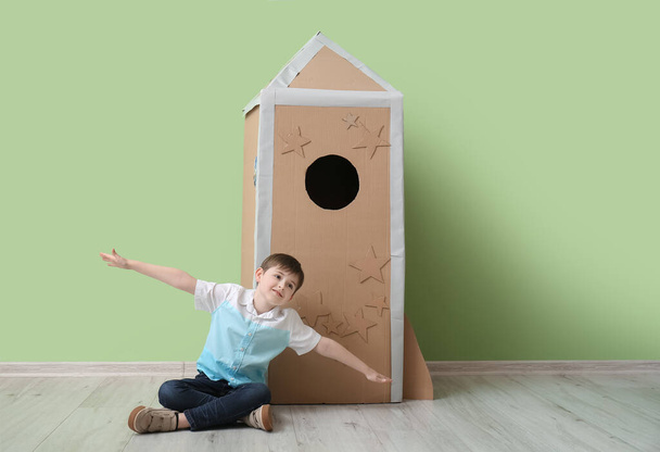Cute little boy playing with cardboard rocket near color wall - Zdjęcie, obraz