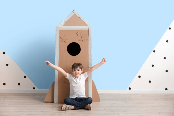Cute little boy playing with cardboard rocket near color wall - Photo, Image