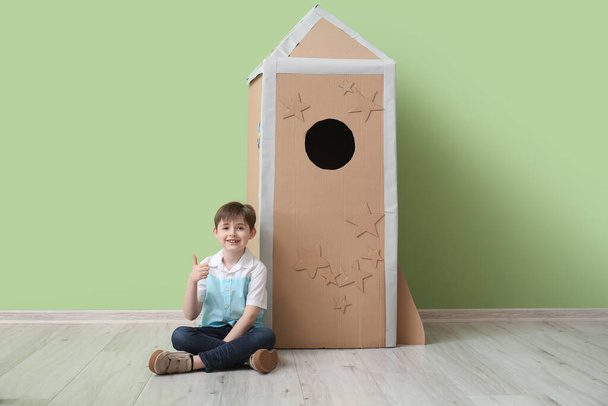 Cute little boy with cardboard rocket showing thumb-up near color wall - Photo, Image