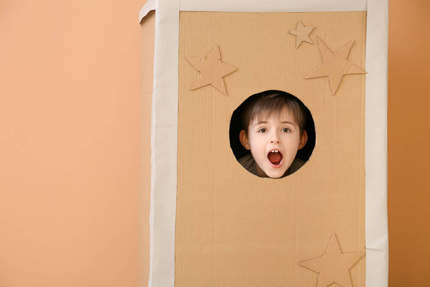 Schockierter kleiner Junge in Papprakete auf farbigem Hintergrund - Foto, Bild