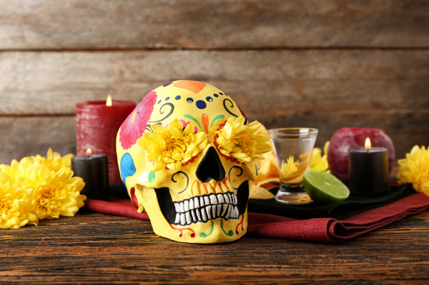 Painted human skull for Mexico's Day of the Dead (El Dia de Muertos), flowers, candles and tequila on wooden background - Photo, Image