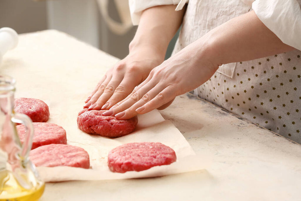 Woman preparing tasty cutlets made of fresh forcemeat at table in kitchen, closeup - Foto, Bild