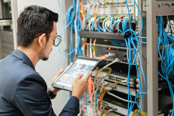 Stock photo of a young network technician holding tablet working to connecting network cables in server cabinet in network server room. IT engineer working in network server room - Φωτογραφία, εικόνα
