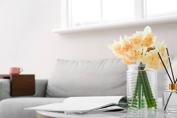 Váza gyönyörű nárcisz, magazin és nád diffúzor az asztalon a szobában - Fotó, kép