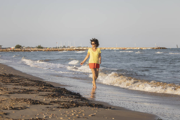 Uma mulher alegre e vital, em seus 70 anos, caminha em uma praia ao pôr do sol, nas margens do Mar Mediterrâneo, Espanha - Foto, Imagem