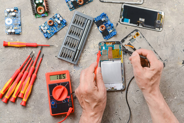 Male technician repairing damaged mobile phone on grunge background - Photo, Image
