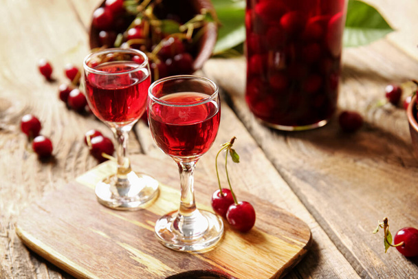Glasses of sweet cherry wine on wooden background - 写真・画像