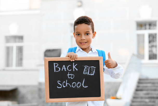 Cute African-American boy holding chalkboard with text BACK TO SCHOOL outdoors - Photo, image