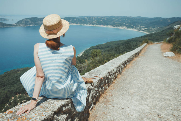 a girl in a hat sits on the parapet and looks at the sea and a beautiful landscap - Zdjęcie, obraz