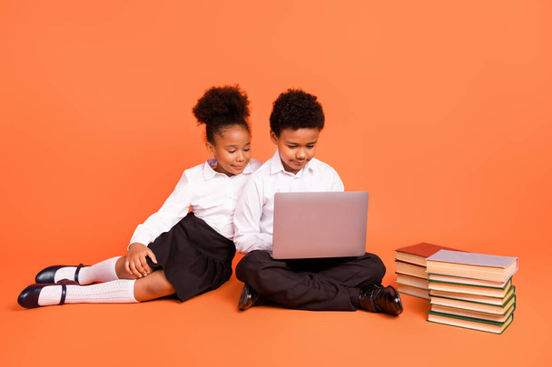Full size photo of two young afro school kids classmates make homework computer isolated over orange color background - Фото, изображение