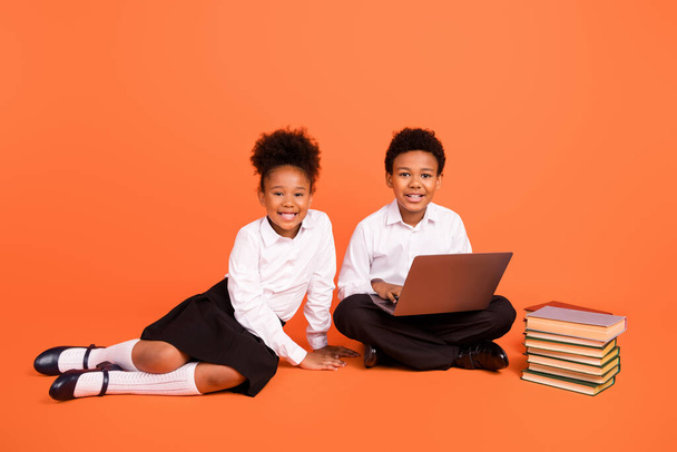 Full length photo of two young afro school kids learn online laptop student isolated over orange color background - 写真・画像