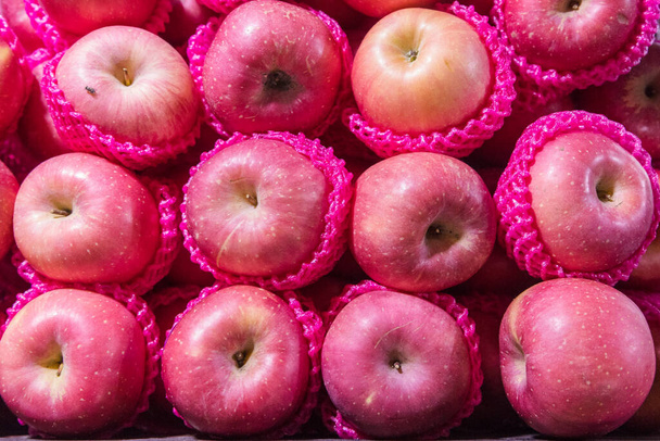 tas de pommes rouges mis ensemble couvrir avec filet de fruits roses regardant de la vue du dessus au marché - Photo, image