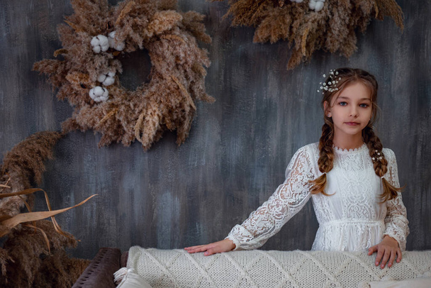 A cute little girl in a beautiful dress at home. Princess with long flowing hair with flowers in retro pastel dress. little lady in a beautiful boho room - Foto, Imagen