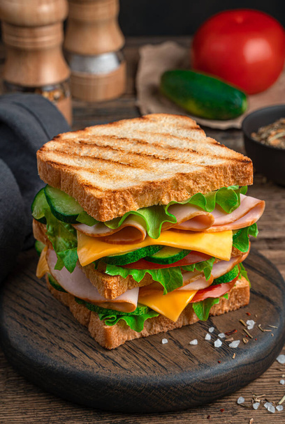 Um grande sanduíche com presunto, queijo, tomate e pepino close-up. Vista lateral. - Foto, Imagem
