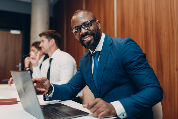 African american black man businessman sitting at table with laptop on office team people background. - 写真・画像