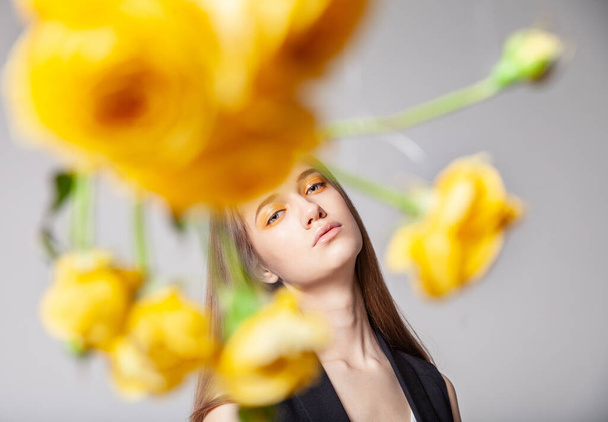 Young woman looking at camera behind yellow flower - Fotoğraf, Görsel