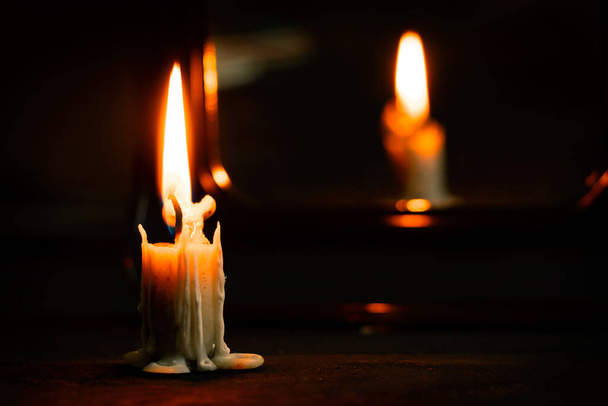 brandende kaars staat op een zwarte houten tafel in het donker bij de spiegel, kaarsvuur in het donker, religie - Foto, afbeelding