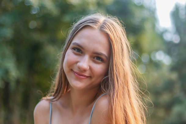 young girl 16 years old, charming brunette with long hair, open smile, against the background of the park, female portrait of a teenager close-up - Photo, Image