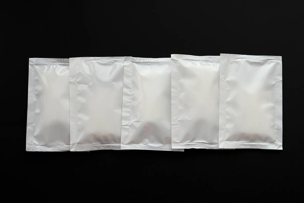 Paquetes de bolsitas blancas en blanco apilan maqueta aislada sobre fondo negro. Embalaje hermético vacío maqueta para salsa, café, toallita húmeda, mayonesa. - Foto, imagen