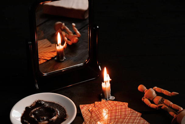 hořící svíčka byla nesena zrcadly a v nedalekém talíři jsou kartičky a kávová sedlina, na černém stolku se ve světle svíček rozezná na kartách jmění - Fotografie, Obrázek
