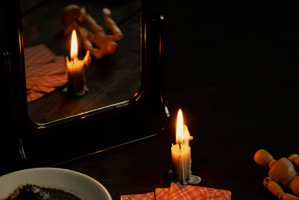 eine brennende Kerze wurde von Spiegeln getragen und in einem Teller in der Nähe liegen Wahrsagerkarten und Kaffeesatz, Wahrsagerkarten bei Kerzenschein auf einem schwarzen Tisch - Foto, Bild