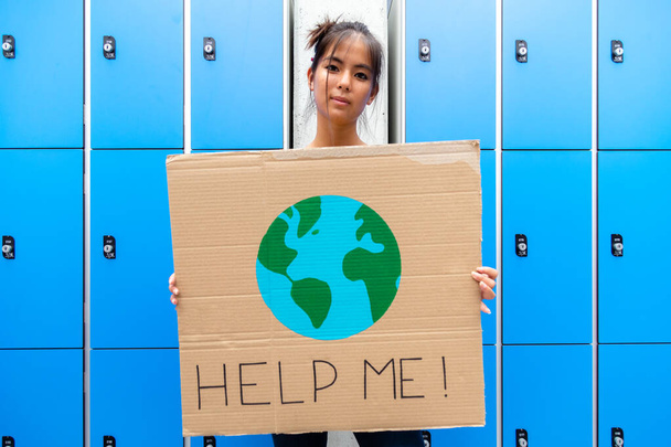 Tiener aziatische middelbare school meisje student kijkend naar camera met een "help me" teken met tekening van planeet Aarde banner. Duurzaamheidsconcept. - Foto, afbeelding