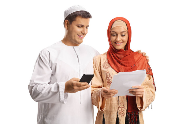 Young man and woman in ethnic clothes holding a paper and using a mobile phone isolated on white background - Fotó, kép
