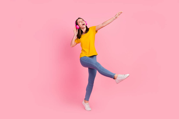 Photo of funky adorable young woman dressed yellow t-shirt walking dancing singing empty space isolated pink color background - Photo, image