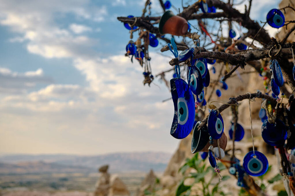 large groups of blue bead worn against the evil eye hanging on trees in edge castle (uchisar) in Cappadocia, gore in Turkey with dramatic cloudscape background - Photo, Image