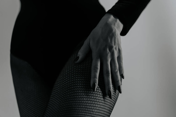 Woman in sexy outfit holds hands on hip. Lady dancer posing, she has slender gorgeous figure. Black fishnet tights and bodysuit. - Foto, imagen