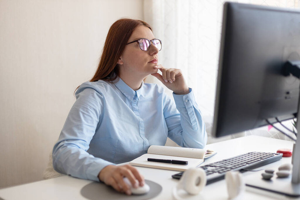 Keskittynyt valkoihoinen amerikkalainen nainen työskentelee ja käyttää tietokonetta toimistossa. - Valokuva, kuva
