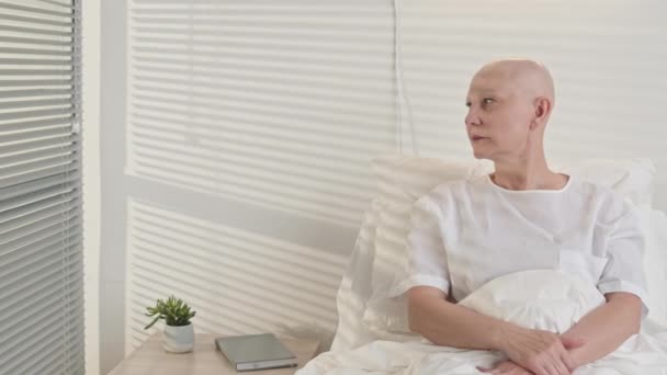 Panning pancia in su colpo di depresso donna matura con il cancro seduto sul letto d'ospedale in camera a fissare un punto pensando alla sua diagnosi - Filmati, video