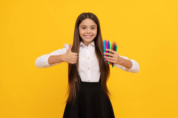 Happy girl child hold felt-tip pens showing thumbs up hand gesture yellow background, satisfied - Photo, Image