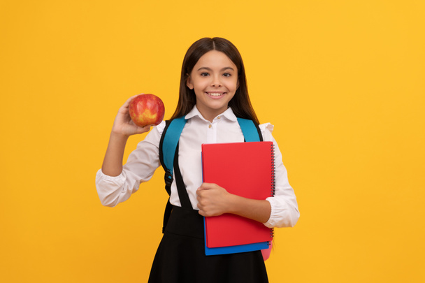 Onnellinen lapsi palaa kouluun mukanaan omena ja kirjoja keltainen tausta, tietopäivä - Valokuva, kuva