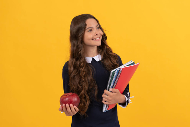 sorridente adolescente menina segurar escola copybooks e maçã almoço no fundo amarelo, de volta à escola. - Foto, Imagem