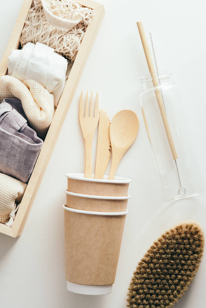 Eco-friendly disposable cardboard tableware, glass water bottle, body brush, cloth shopping bags on white background. Flat lay, top view - Φωτογραφία, εικόνα